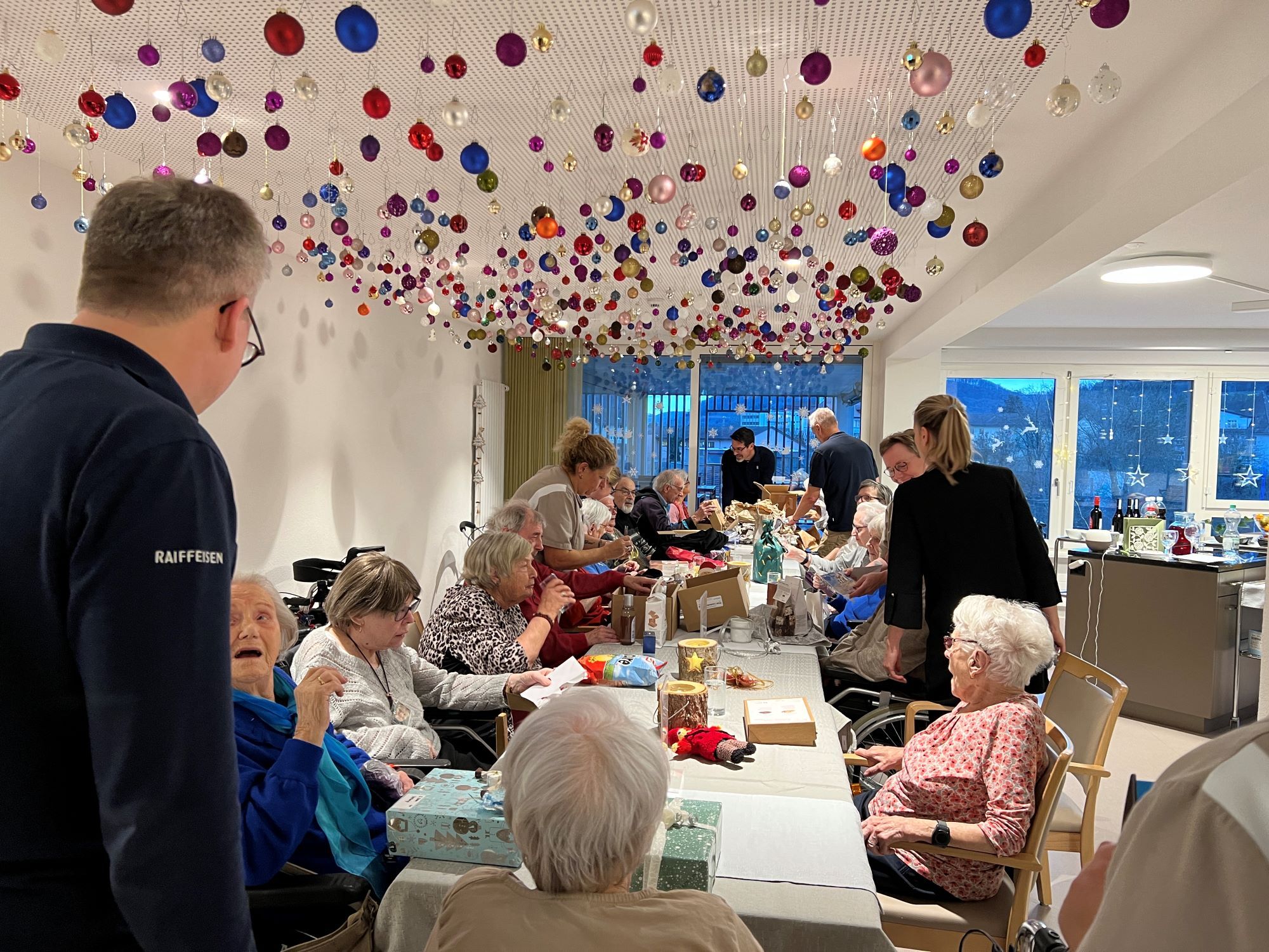 Raiffeisenbank Mitarbeiter übergibt ein Weihnachtsgeschenk an eine Seniorin im Rollstuhl
