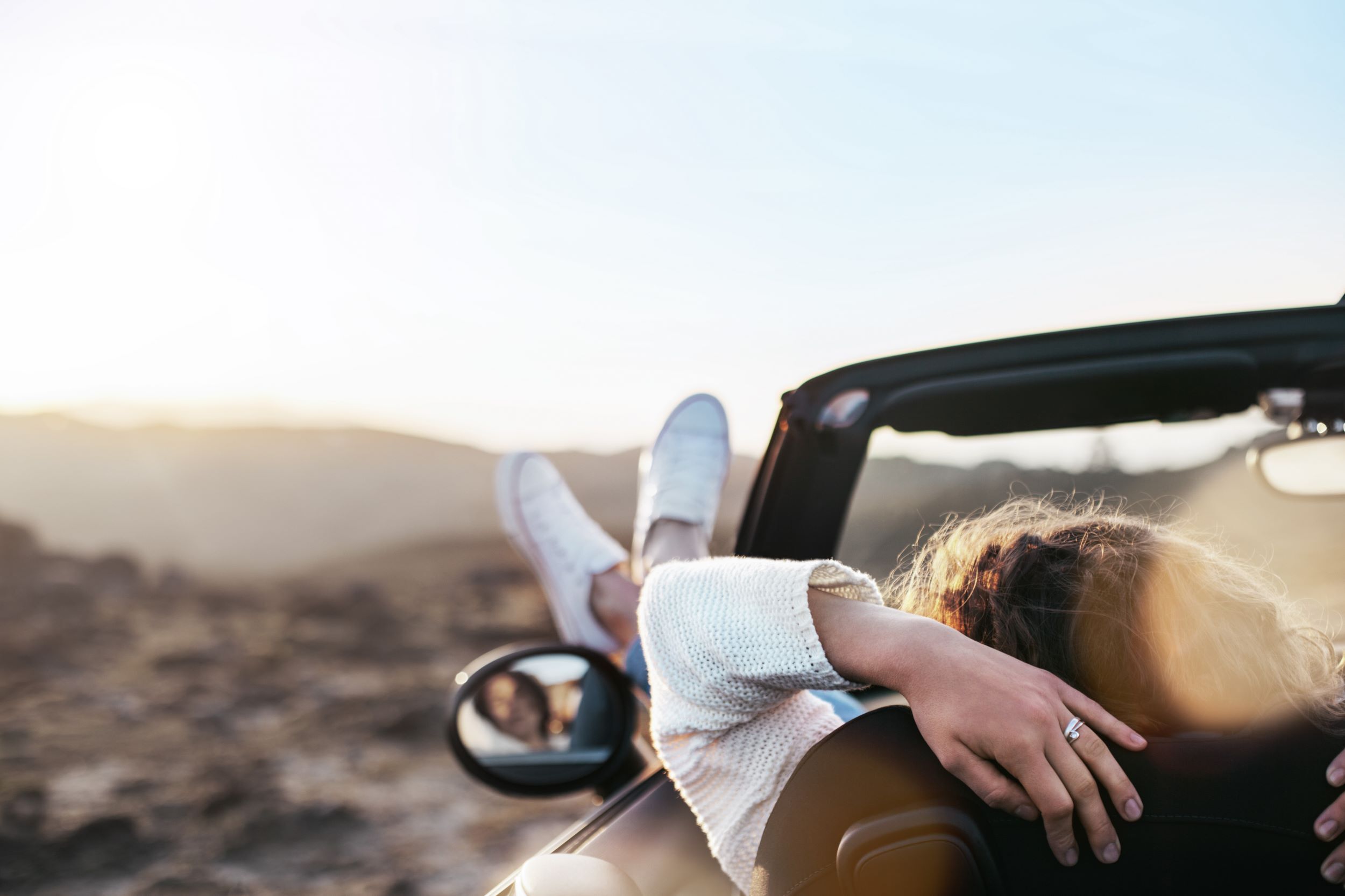 Bild einer im Cabriolet sitzenden Frau mit Füsse aus dem Fenster.