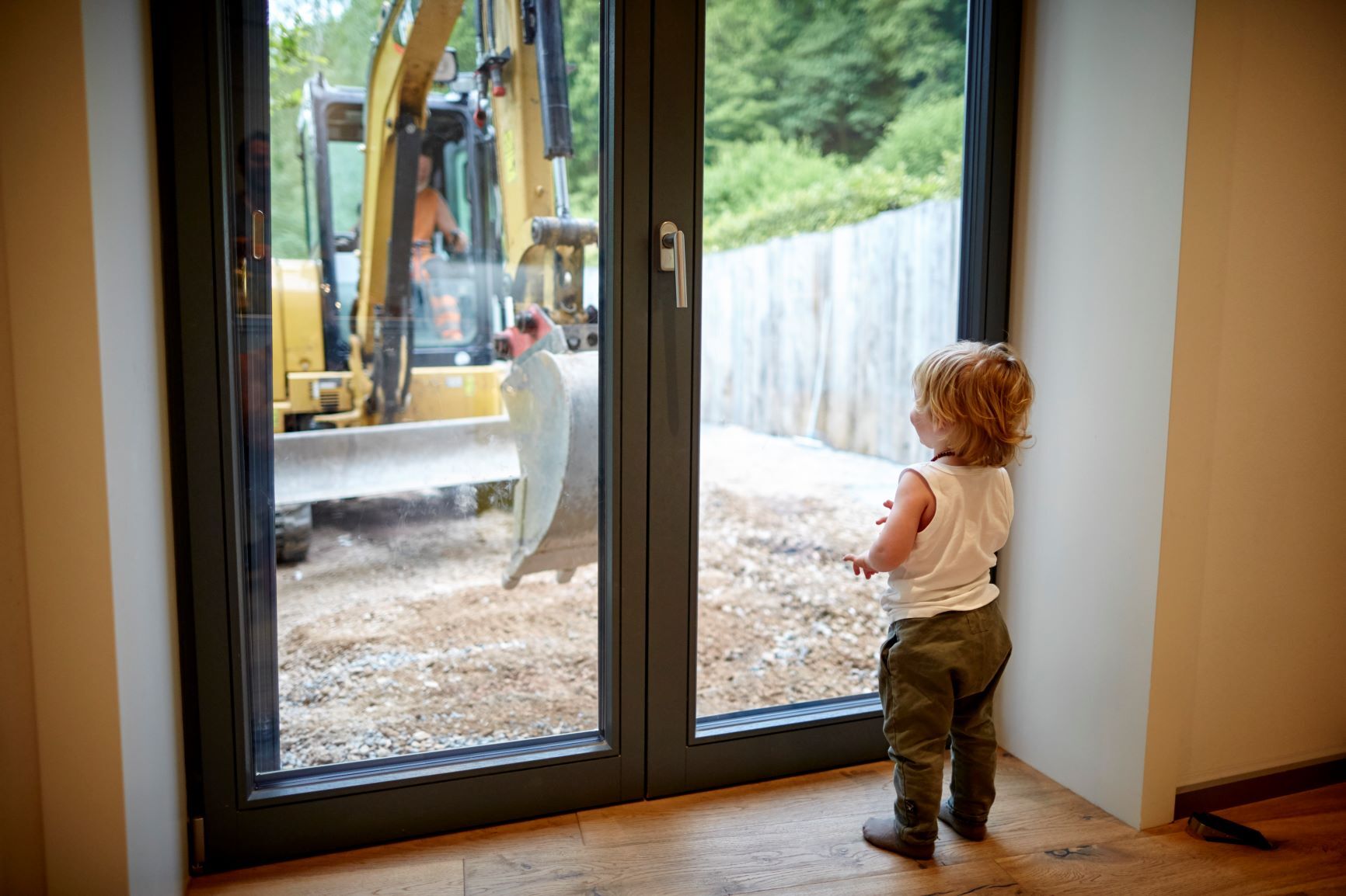 Kind steht vor Fenster und schaut einem Bagger zu